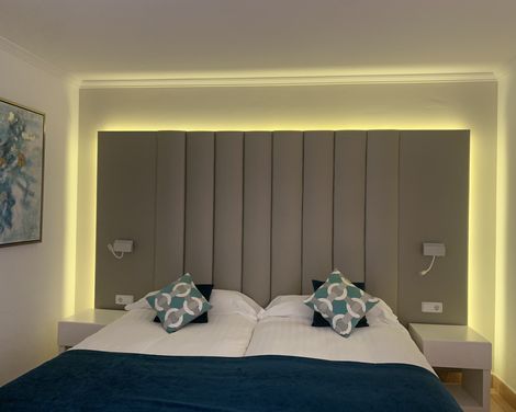 Modernes Hotelzimmer mit Doppelbett, indirekt beleuchtetem Kopfteil und türkisfarbenen Akzenten.