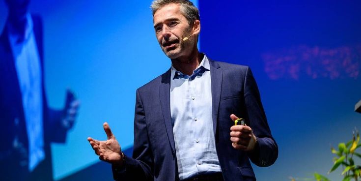 Mann in Anzug spricht auf einer Bühne mit Mikrofon und Gestik – Symbol für Vortrag zu Nachhaltigkeit und Zukunftsthemen.