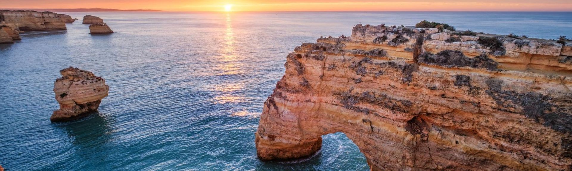 Goldfarbene Felsklippen und natürliche Steinbögen an der Algarve bei Sonnenuntergang.