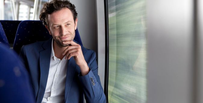 Geschäftsmann sitzt nachdenklich am Fenster eines Zuges.